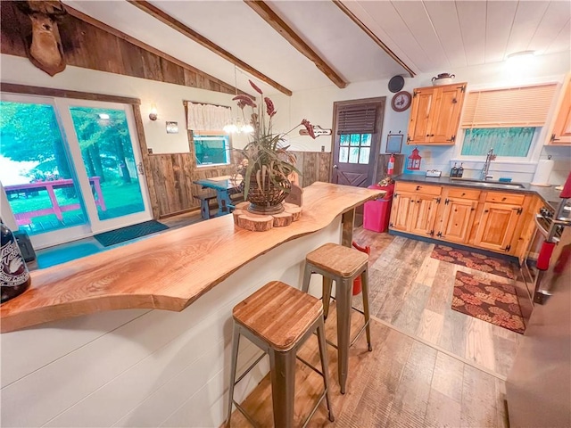 kitchen featuring sink, vaulted ceiling with beams, light hardwood / wood-style floors, a breakfast bar area, and wood walls