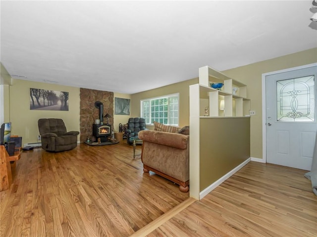 living room featuring light hardwood / wood-style floors, a wood stove, and a baseboard heating unit