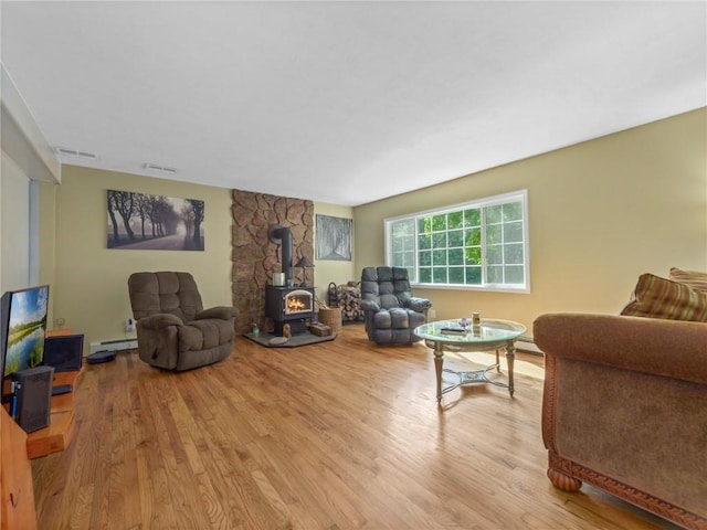 living room with a wood stove, a baseboard heating unit, and light wood-type flooring