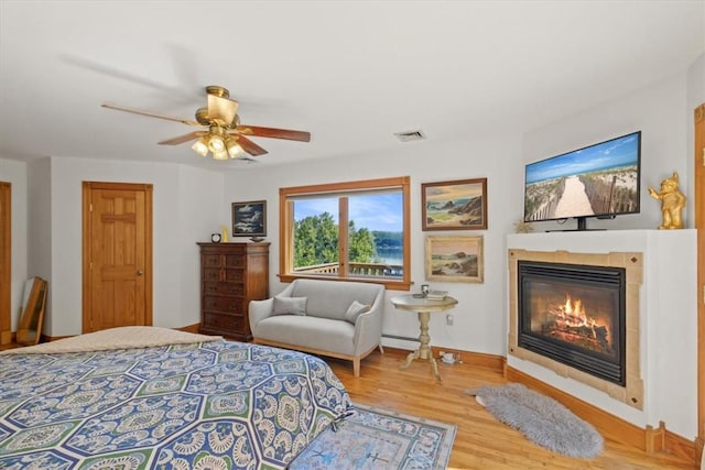 bedroom with visible vents, a ceiling fan, a glass covered fireplace, wood finished floors, and baseboards