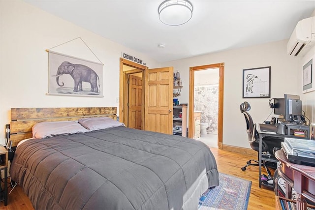 bedroom with wood finished floors, baseboards, ensuite bathroom, and a wall mounted AC