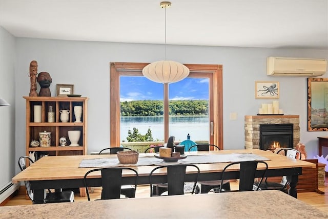 dining area featuring a fireplace, light wood finished floors, a water view, a baseboard heating unit, and an AC wall unit