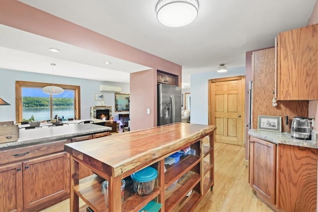 kitchen featuring brown cabinets, a fireplace, stainless steel refrigerator with ice dispenser, light wood-style flooring, and a wall mounted air conditioner