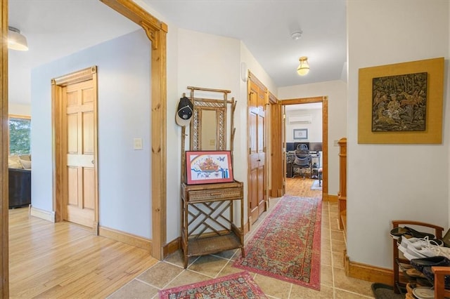 corridor featuring a wall mounted AC, light tile patterned flooring, and baseboards