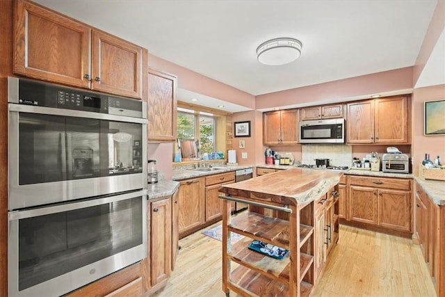 kitchen featuring stainless steel appliances, a sink, light wood-style floors, decorative backsplash, and brown cabinetry