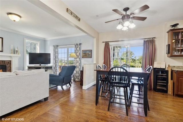 dining room featuring dark hardwood / wood-style flooring, ceiling fan, crown molding, a fireplace, and wine cooler