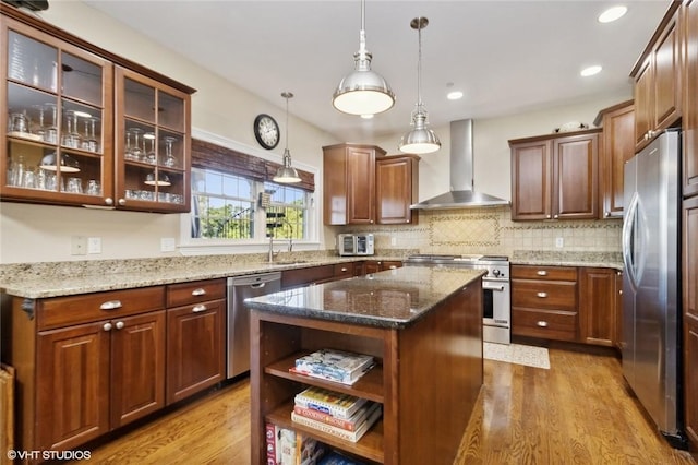 kitchen featuring a center island, hanging light fixtures, wall chimney exhaust hood, appliances with stainless steel finishes, and light hardwood / wood-style floors