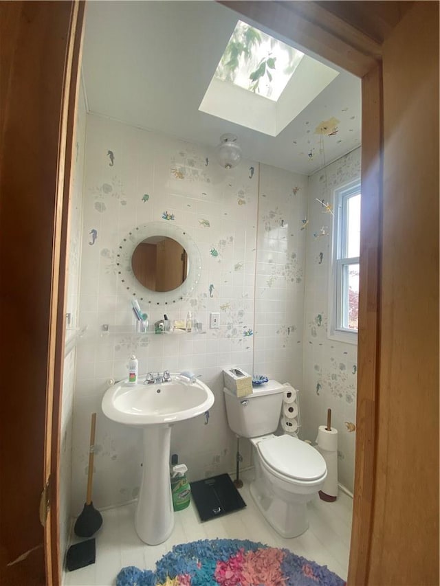 bathroom with tile patterned floors, sink, a skylight, toilet, and tile walls