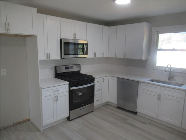 kitchen with backsplash, stainless steel appliances, sink, light hardwood / wood-style flooring, and white cabinetry