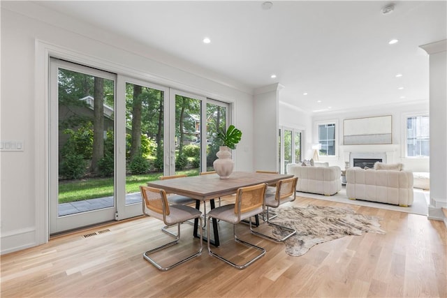 dining room with light wood-type flooring, a wealth of natural light, and crown molding