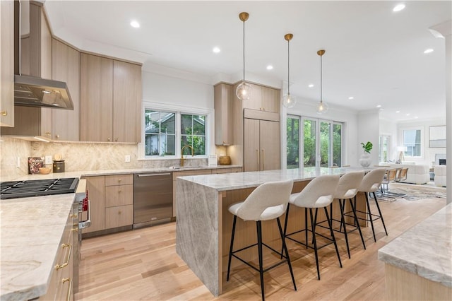 kitchen with wall chimney exhaust hood, plenty of natural light, light brown cabinets, and appliances with stainless steel finishes