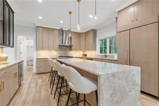 kitchen featuring light wood-type flooring, a center island, ornamental molding, and wall chimney range hood