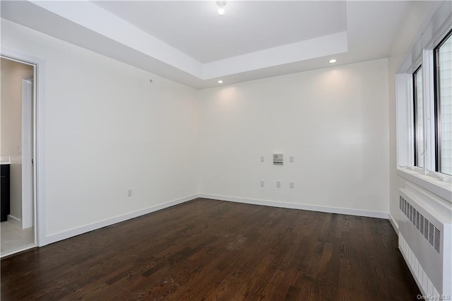 unfurnished room featuring dark hardwood / wood-style flooring, a tray ceiling, and radiator