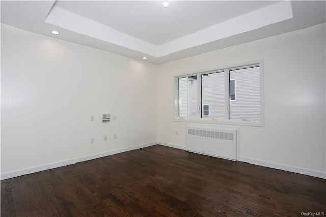 spare room featuring a tray ceiling, radiator heating unit, and dark hardwood / wood-style floors