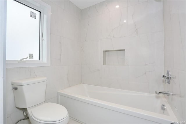 bathroom with tiled shower / bath, toilet, and tile walls