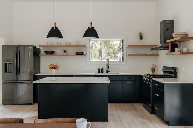 kitchen with light wood-type flooring, sink, black gas stove, stainless steel fridge with ice dispenser, and hanging light fixtures