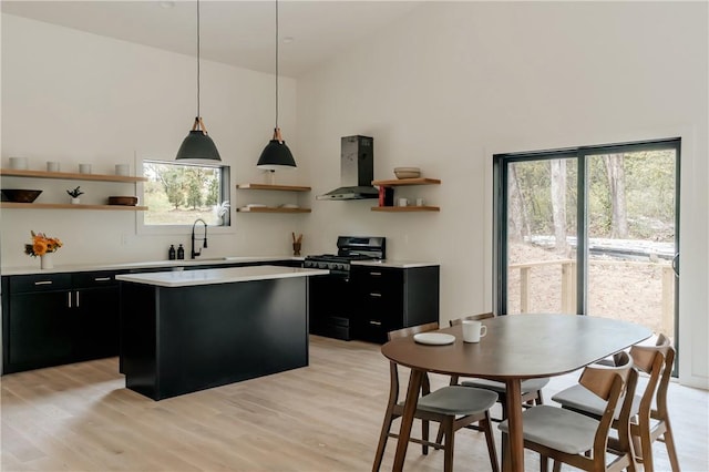 kitchen with light hardwood / wood-style floors, a healthy amount of sunlight, wall chimney range hood, and black gas range oven