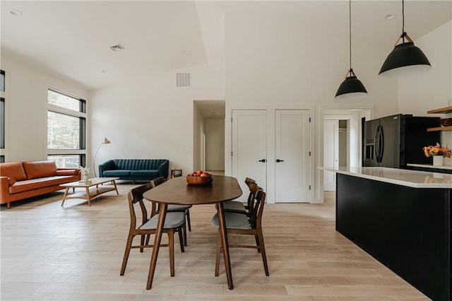 dining space featuring light wood-type flooring and high vaulted ceiling