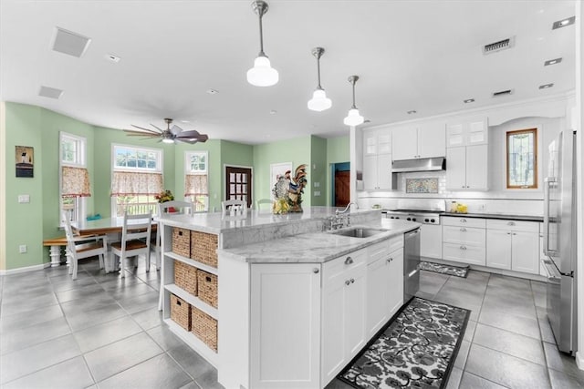 kitchen with decorative light fixtures, white cabinetry, an island with sink, sink, and light stone countertops