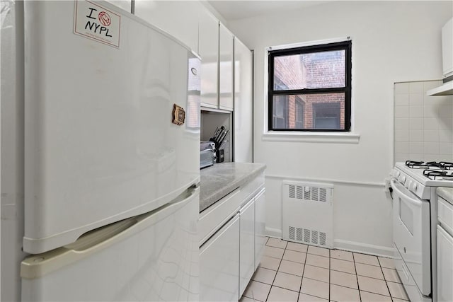 kitchen featuring white cabinetry, light tile patterned floors, white appliances, and radiator