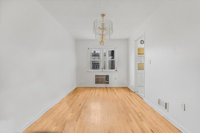 unfurnished room featuring heating unit, light hardwood / wood-style flooring, and an inviting chandelier