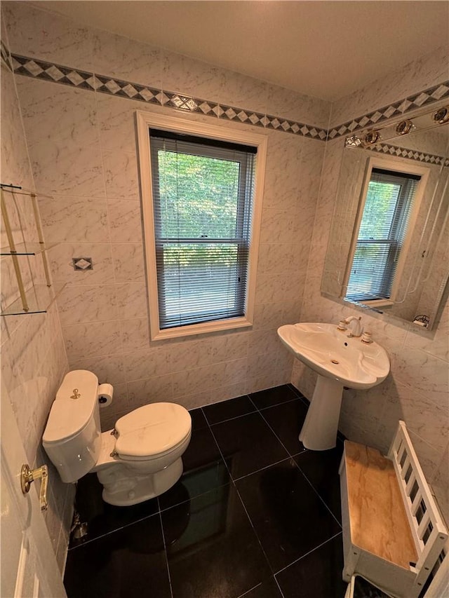 bathroom with toilet, tile walls, and a healthy amount of sunlight