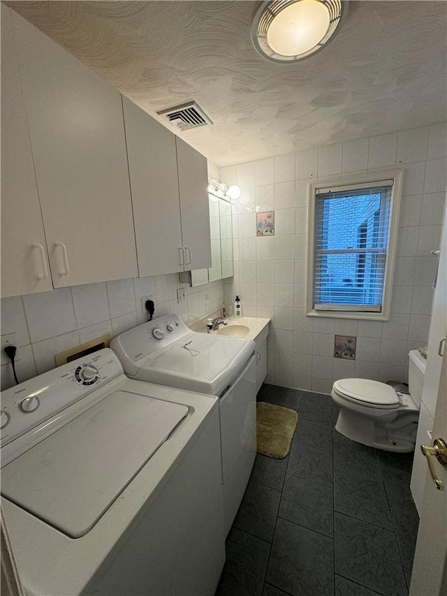 laundry area with a textured ceiling, dark tile patterned floors, tile walls, and washing machine and clothes dryer