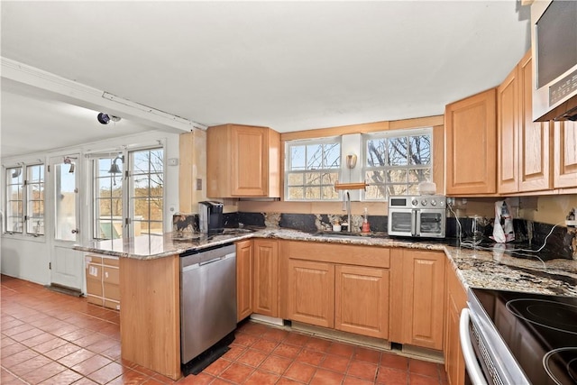 kitchen with sink, tile patterned flooring, kitchen peninsula, stone countertops, and appliances with stainless steel finishes