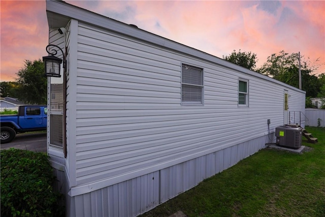 property exterior at dusk with central air condition unit and a lawn