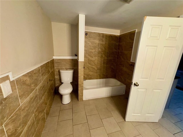 bathroom with tile patterned floors, toilet, washtub / shower combination, and tile walls