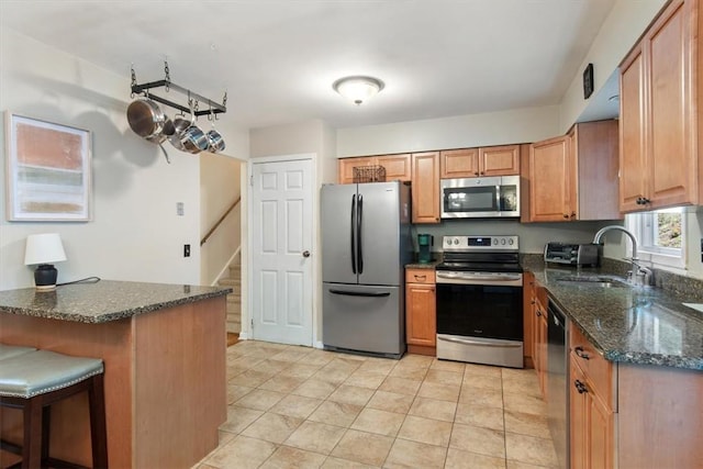 kitchen featuring sink, stainless steel appliances, kitchen peninsula, dark stone counters, and a kitchen bar