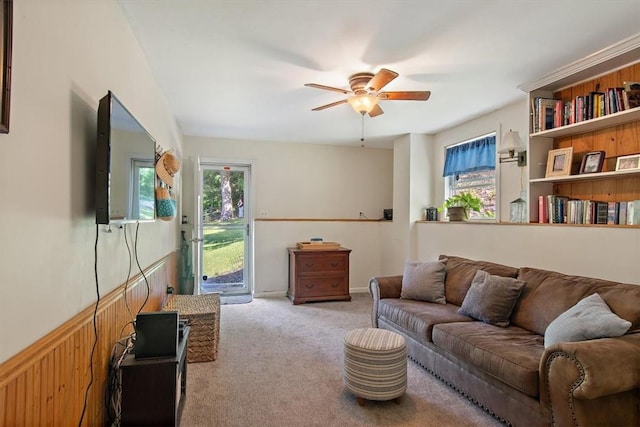 carpeted living room with ceiling fan and wooden walls