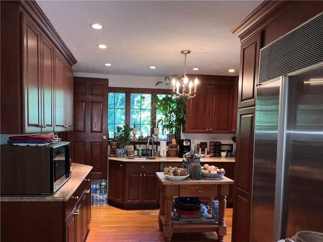 kitchen with stainless steel appliances, sink, decorative light fixtures, light hardwood / wood-style flooring, and a chandelier