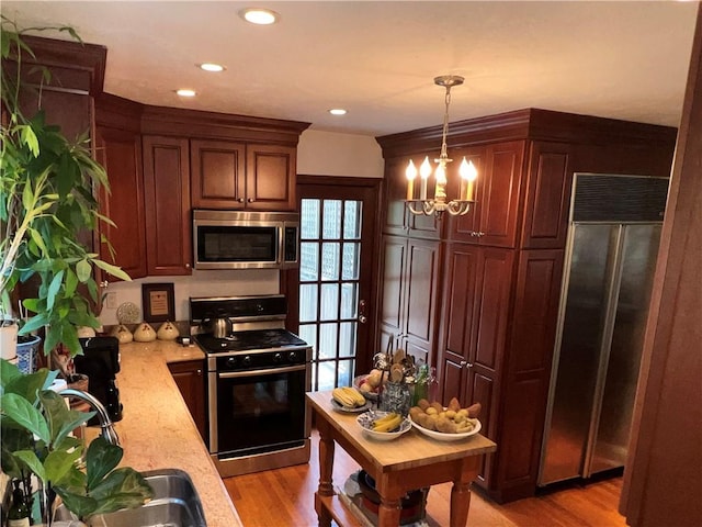 kitchen with light stone countertops, hanging light fixtures, stainless steel appliances, an inviting chandelier, and light hardwood / wood-style flooring