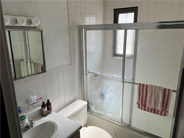 full bathroom featuring vanity, bath / shower combo with glass door, toilet, tile walls, and tasteful backsplash