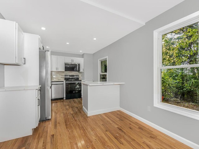 kitchen with kitchen peninsula, light wood-type flooring, tasteful backsplash, stainless steel appliances, and white cabinetry