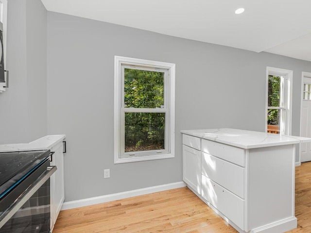 kitchen with light stone countertops, kitchen peninsula, white cabinetry, and light hardwood / wood-style floors