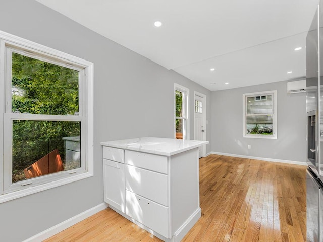 kitchen with white cabinets, light hardwood / wood-style floors, a wall unit AC, and light stone counters