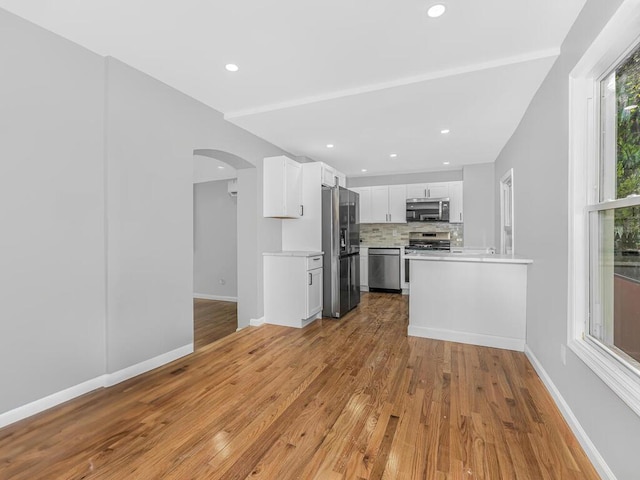 kitchen with white cabinets, decorative backsplash, appliances with stainless steel finishes, and light hardwood / wood-style flooring