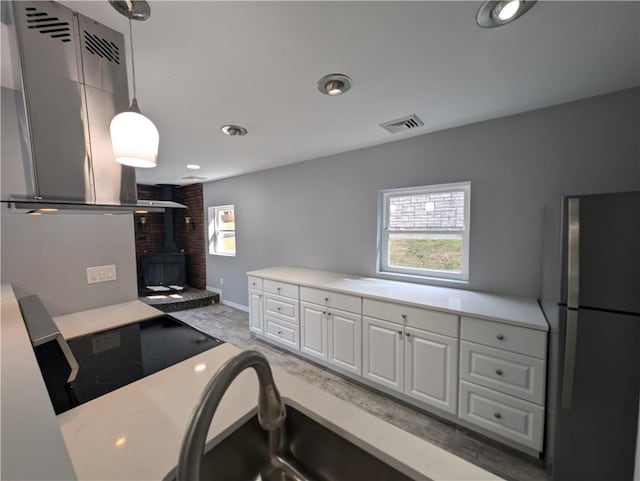 kitchen featuring a wood stove, cooktop, stainless steel fridge, pendant lighting, and white cabinets