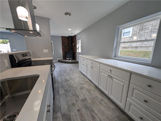 kitchen featuring a wood stove, white cabinetry, sink, hardwood / wood-style floors, and pendant lighting