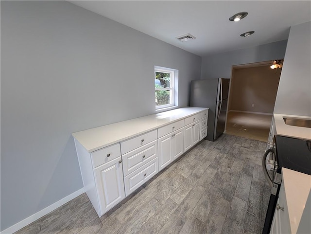 kitchen with white cabinets, black range, light wood-type flooring, and stainless steel refrigerator