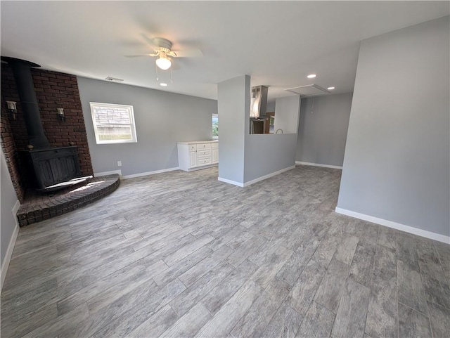 unfurnished living room with a wood stove, ceiling fan, and light hardwood / wood-style flooring