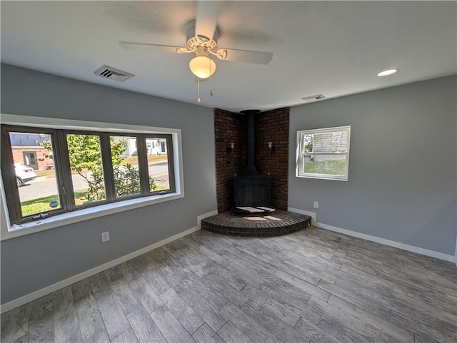 unfurnished living room with hardwood / wood-style floors, ceiling fan, a healthy amount of sunlight, and a wood stove