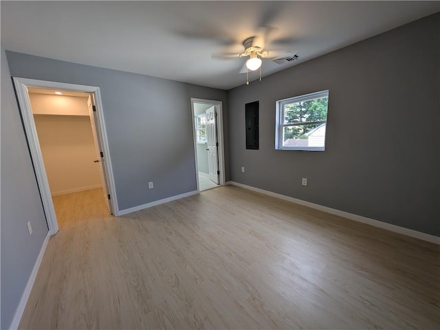 unfurnished bedroom with ceiling fan, electric panel, light hardwood / wood-style floors, a walk in closet, and a closet