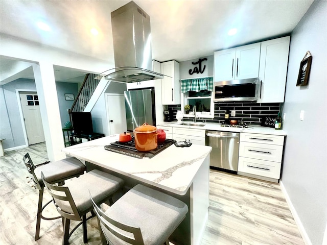 kitchen featuring sink, light wood-type flooring, appliances with stainless steel finishes, white cabinetry, and island exhaust hood