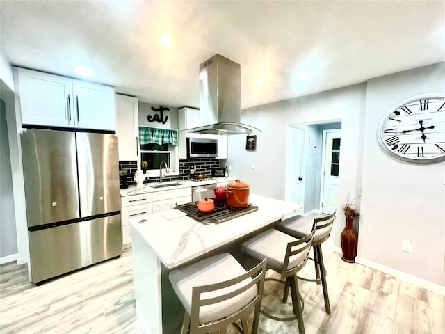 kitchen with light stone counters, light hardwood / wood-style floors, island range hood, white cabinets, and appliances with stainless steel finishes