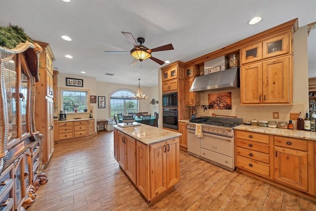 kitchen featuring a center island, wall chimney range hood, light stone counters, black appliances, and light wood-type flooring