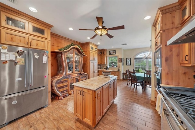 kitchen with ceiling fan, stainless steel appliances, range hood, a kitchen island, and light wood-type flooring