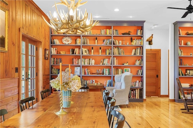 living area featuring ceiling fan with notable chandelier, light wood-type flooring, wooden walls, and french doors